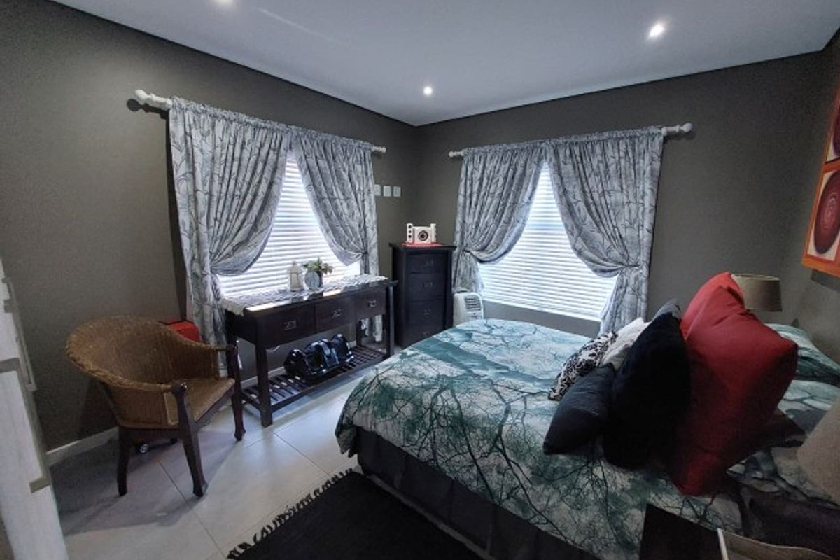 A well-maintained bedroom featuring tiled flooring, recessed downlighting, and dual windows fitted with curtain rods and venetian blinds.
