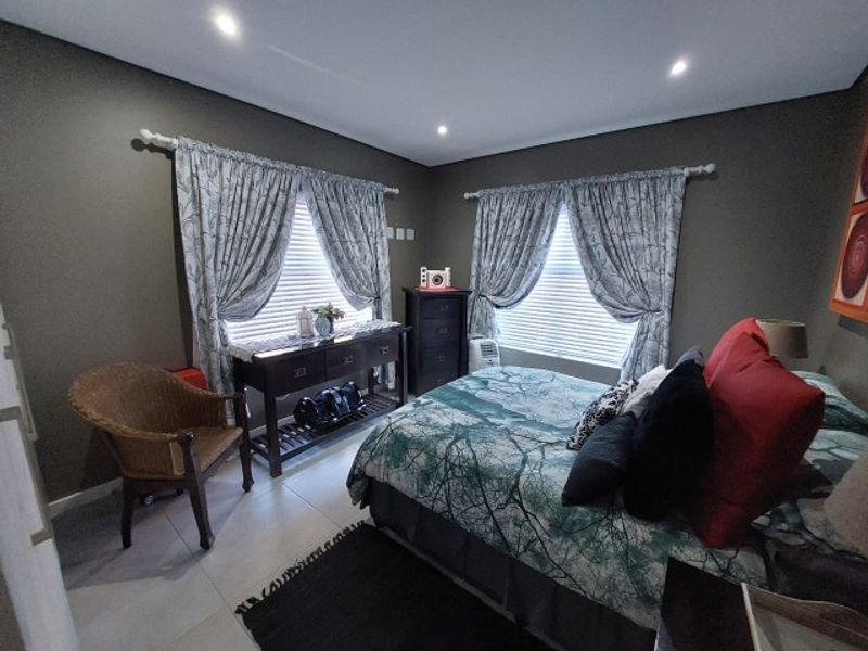 A well-maintained bedroom featuring tiled flooring, recessed downlighting, and dual windows fitted with curtain rods and venetian blinds.