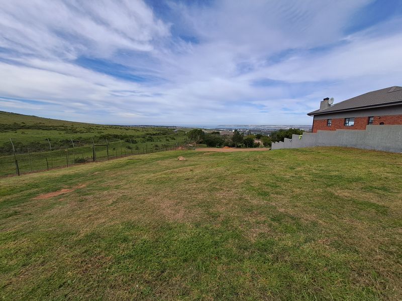 Spacious rear yard of a residential property featuring a manicured lawn, perimeter electric fencing, and a view of the surrounding landscape.