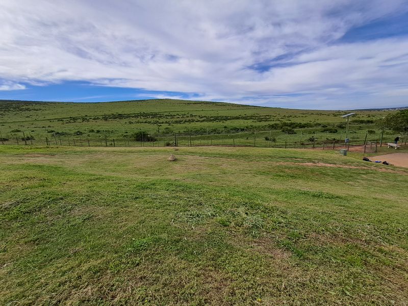 A wide-angle view of a grassy vacant residential plot featuring perimeter wire fencing and a solar light pole against a hilly landscape.