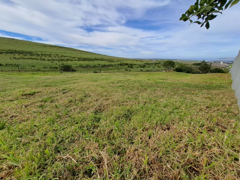 A wide-angle view of the vacant residential land featuring natural grass terrain and perimeter fencing with distant coastal landscape views.