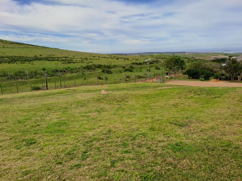 A wide-angle view of a vacant residential plot featuring grassy terrain, perimeter fencing, and distant coastal landscape views.
