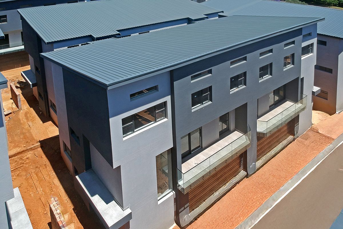 Aerial view of a modern townhouse complex featuring contemporary grey facades, metal roofing, and glass-fronted balconies, currently in the final stages of construction.