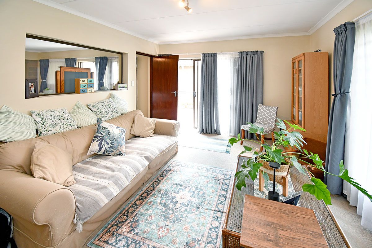 A comfortable living room featuring neutral wall tones, carpeted flooring, and a large interior window opening, with direct access to an outdoor patio area.