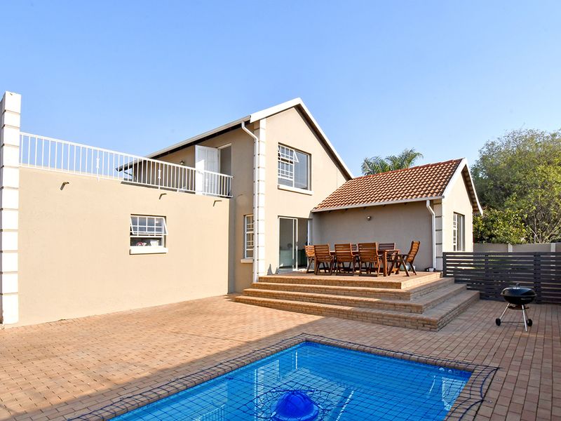 Rear exterior view featuring a paved patio area, swimming pool with safety net, and an elevated balcony accessible from the upper level.