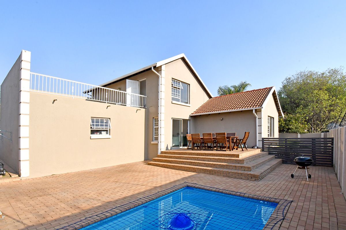 Rear exterior view featuring a paved patio area, swimming pool with safety net, and an elevated balcony accessible from the upper level.