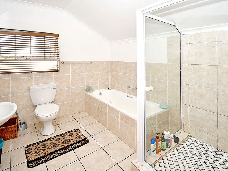 A functional bathroom featuring a pedestal basin, toilet, built-in bathtub, and a separate glass-enclosed shower with neutral tiled finishes.