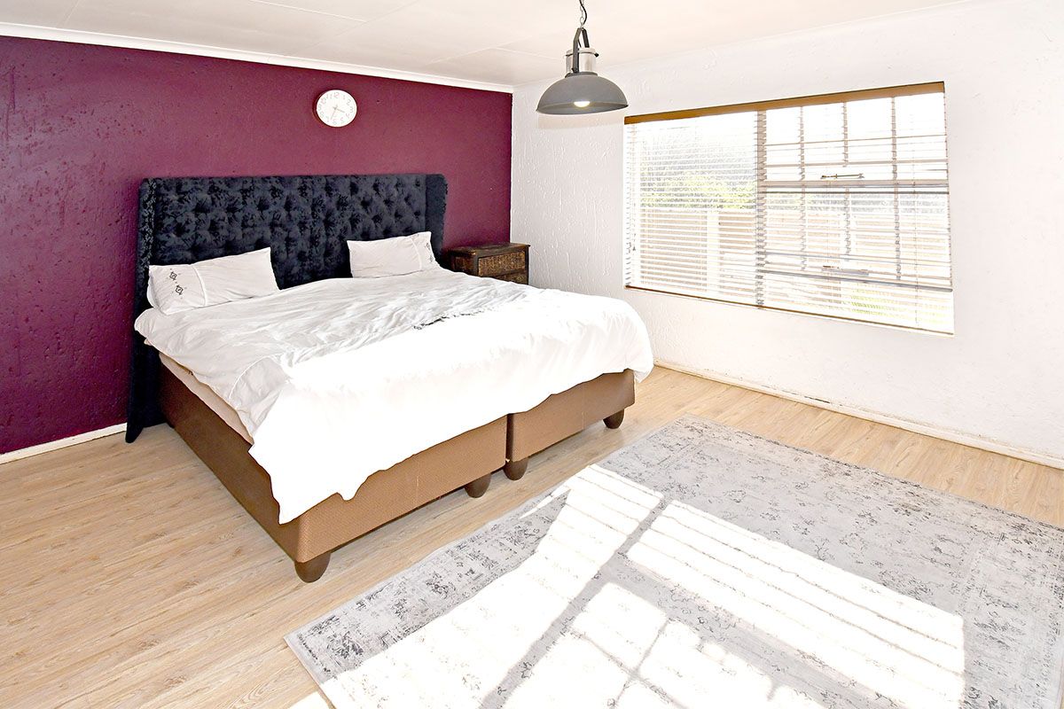 A bedroom featuring laminate flooring, a pendant light fixture, and venetian blinds, with a bold accent wall.