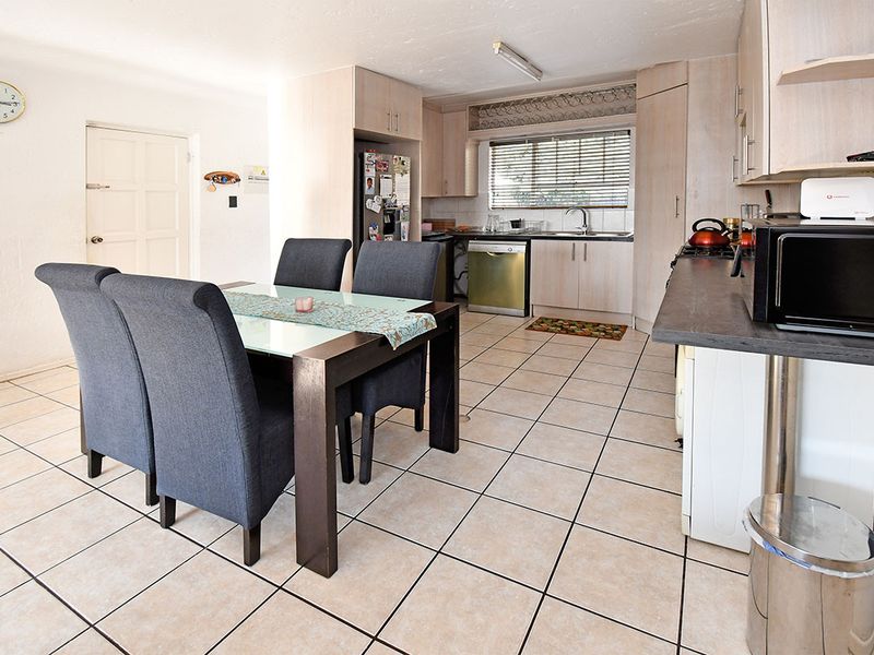 Open plan kitchen and dining area featuring tiled flooring, light wood-finish cabinetry, and dark laminate countertops.