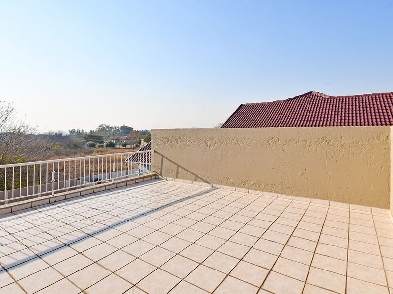 An open-air balcony featuring tiled flooring, a metal balustrade, and a masonry privacy wall, offering elevated views of the surrounding landscape.