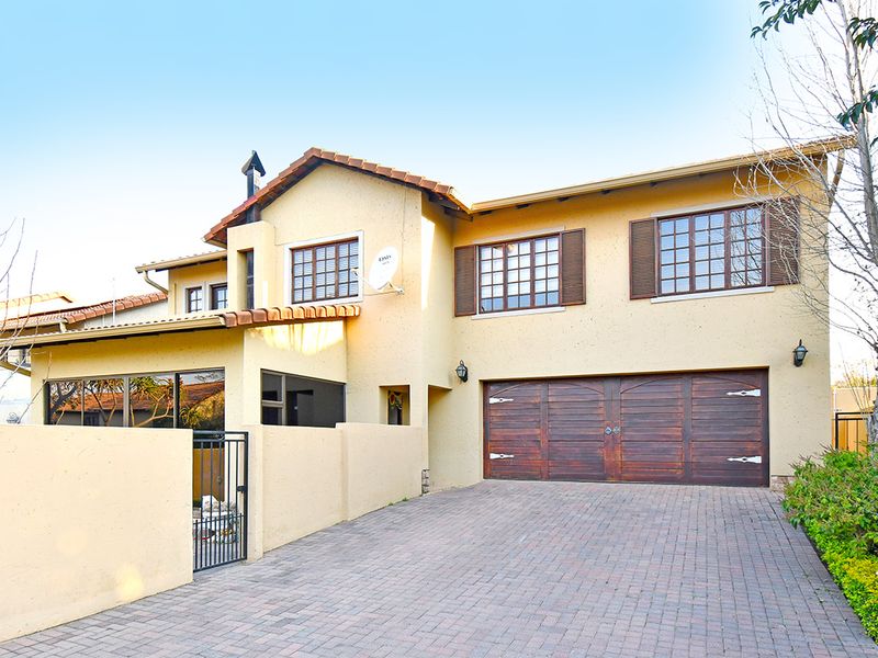 Front elevation of a two-story house featuring a paved driveway, double wooden garage doors, and classic terracotta roof tiles.