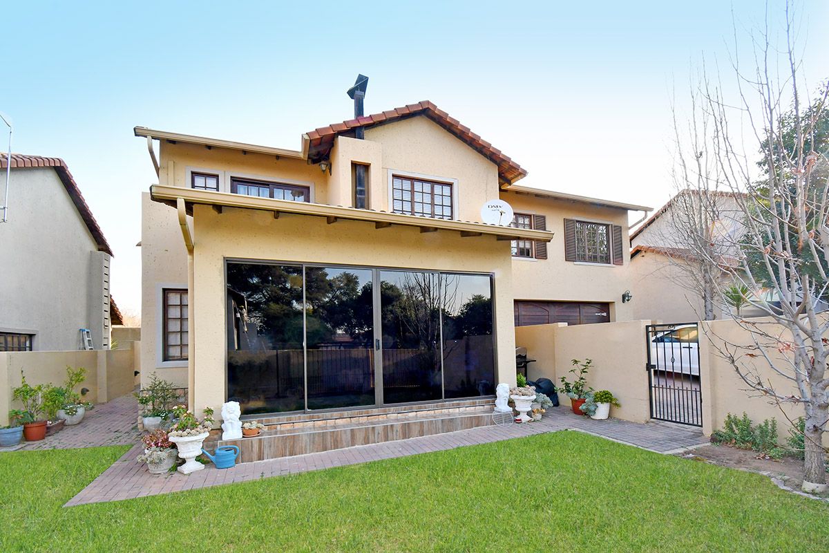 Rear view of a two-story house featuring a tiled roof, large sliding glass doors leading to a tiled patio, and a private garden area.