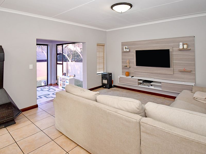 Spacious living room featuring tiled flooring, a modern built-in media unit, and a freestanding fireplace, with direct access to an outdoor patio area.