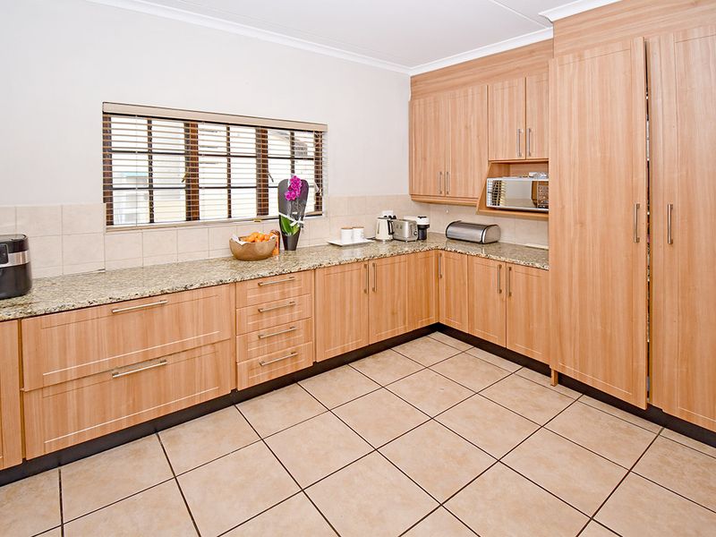 A functional kitchen featuring light wood-tone cabinetry, granite countertops, tiled backsplash, and ceramic floor tiles with a built-in microwave.