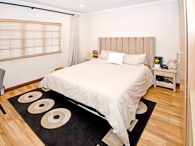 A well-maintained bedroom featuring wood-look tile flooring, neutral walls, and a built-in wardrobe, offering a comfortable and functional living space.