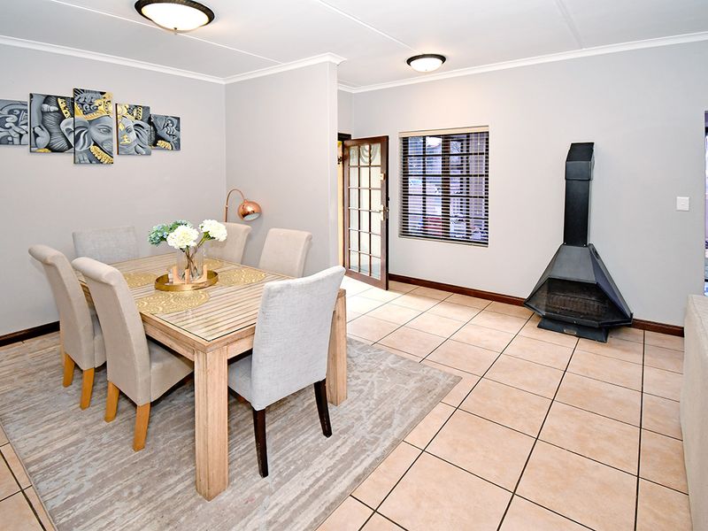 A bright dining area featuring neutral tiled flooring, a freestanding fireplace, and direct access to an exterior space through a timber-framed glass door.