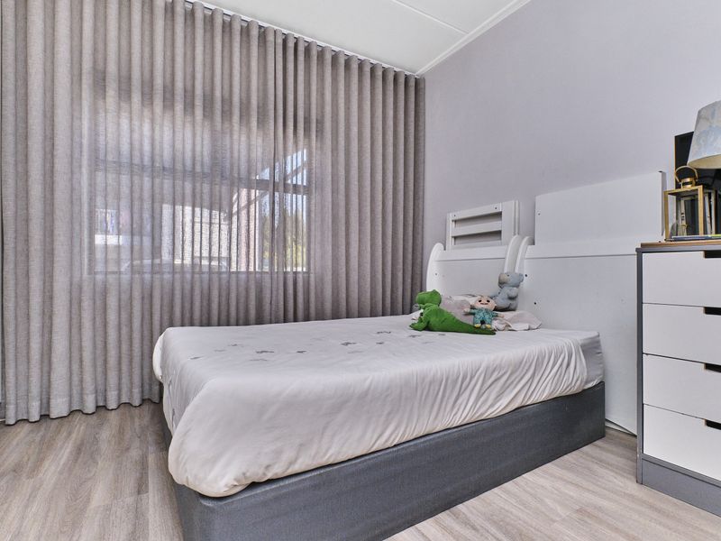 A well-maintained bedroom featuring light-toned laminate flooring, a built-in wardrobe, and floor-to-ceiling curtains providing natural light control.