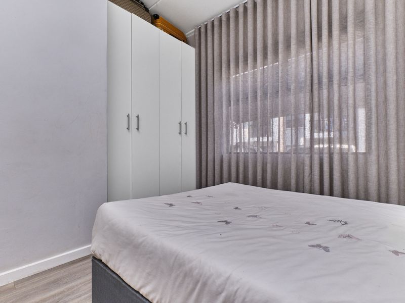 A well-maintained bedroom featuring neutral laminate flooring, a modern white built-in wardrobe, and floor-to-ceiling window treatments.