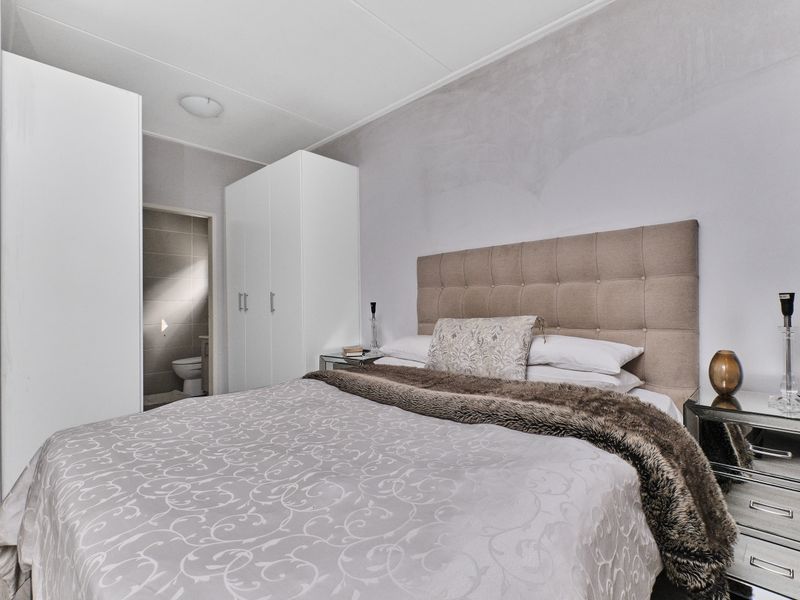 A well-maintained bedroom featuring built-in wardrobes and neutral finishes, with an adjoining bathroom visible through the doorway.