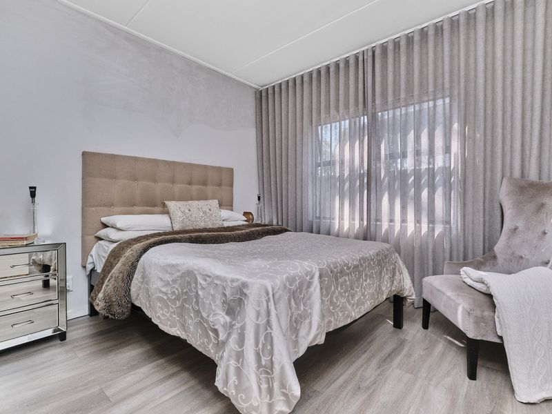 A well-lit bedroom featuring light-toned laminate flooring and floor-to-ceiling curtains, providing a neutral foundation for personal styling.