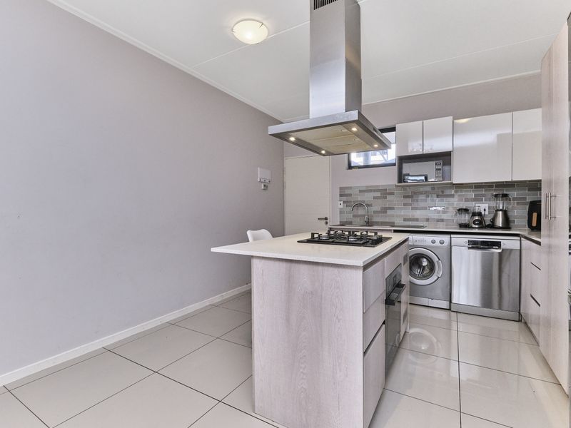 Modern kitchen featuring a central island with gas hob, stainless steel extractor, subway tile backsplash, and sleek cabinetry with integrated appliances.