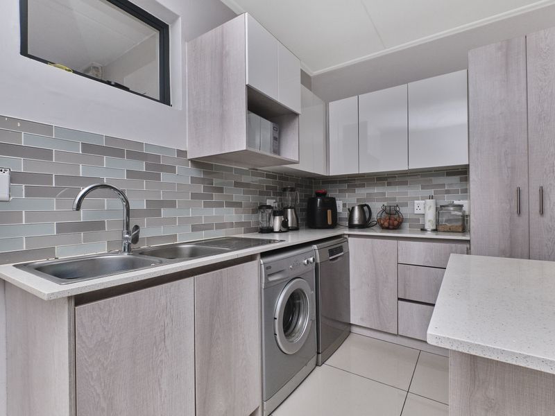 Modern kitchen featuring light wood-grain cabinetry, stone countertops, a stylish subway tile backsplash, and integrated laundry and dishwasher appliances.