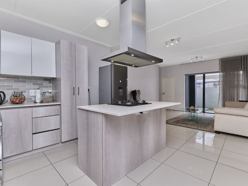 Modern open-plan kitchen and living area featuring a central island with gas hob, sleek cabinetry, tiled floors, and direct access to an outdoor patio.