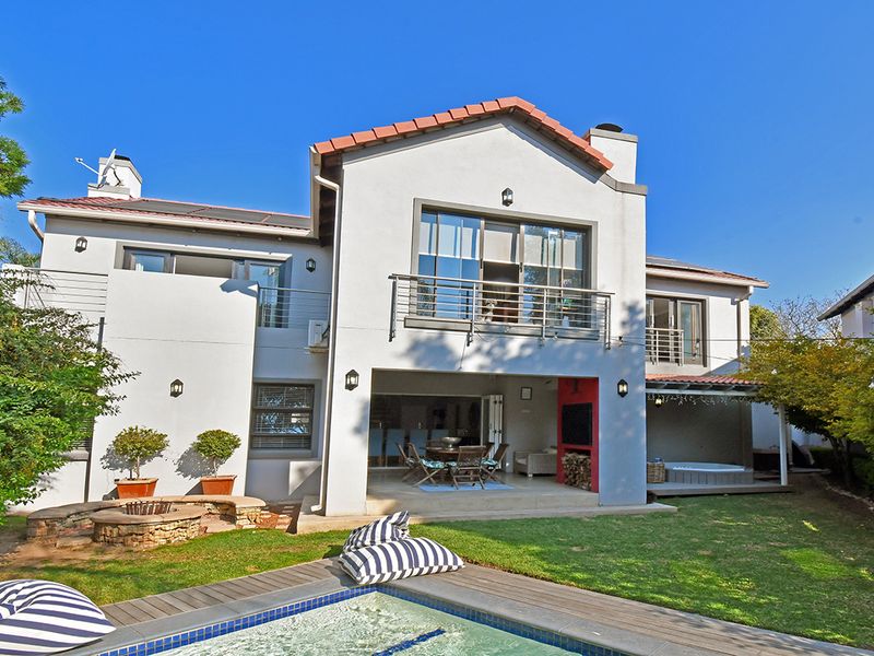Rear view of a multi-story house featuring a swimming pool, stone fire pit, covered patio with built-in fireplace, and upper-level balconies.