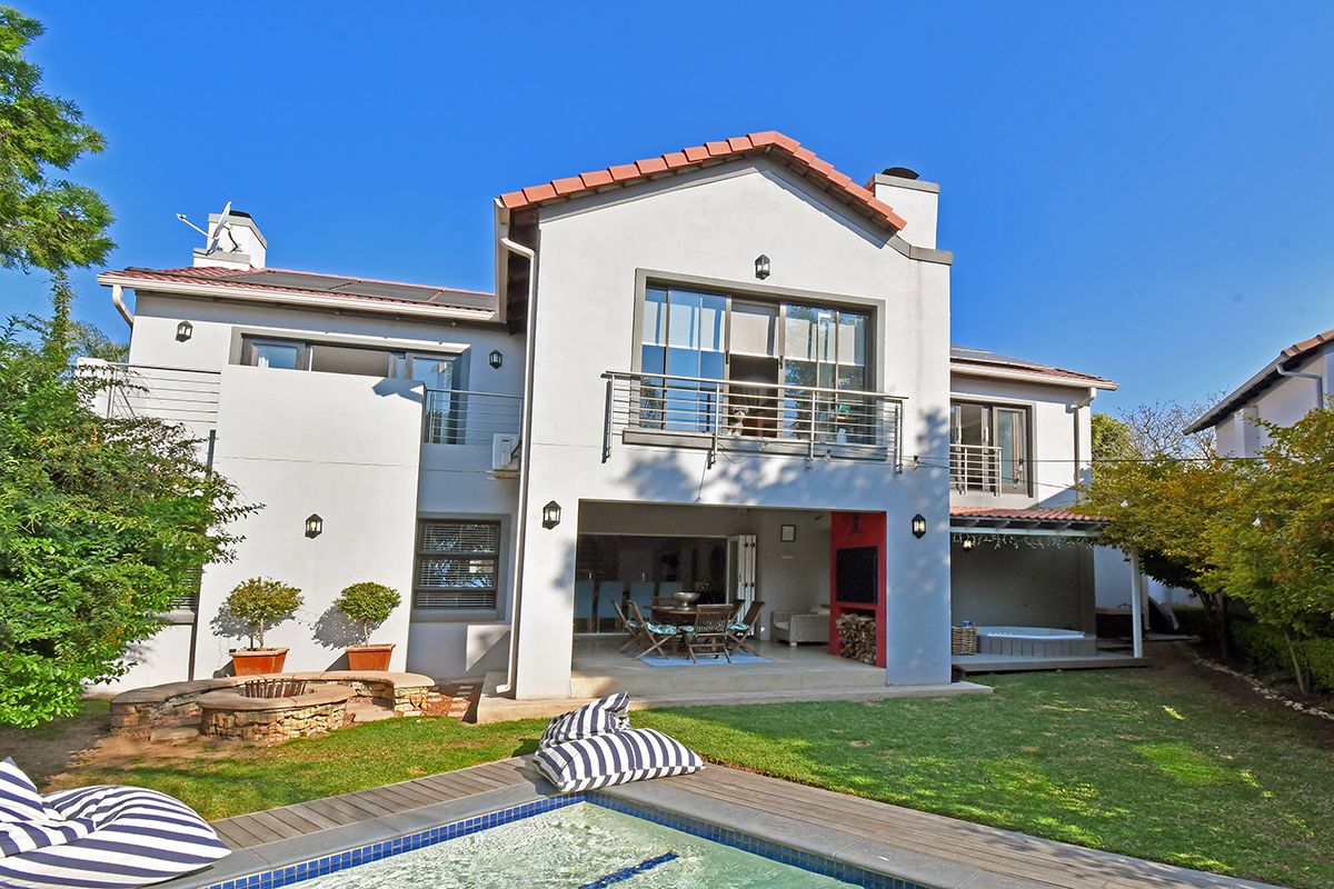 Rear view of a multi-story house featuring a swimming pool, stone fire pit, covered patio with built-in fireplace, and upper-level balconies.