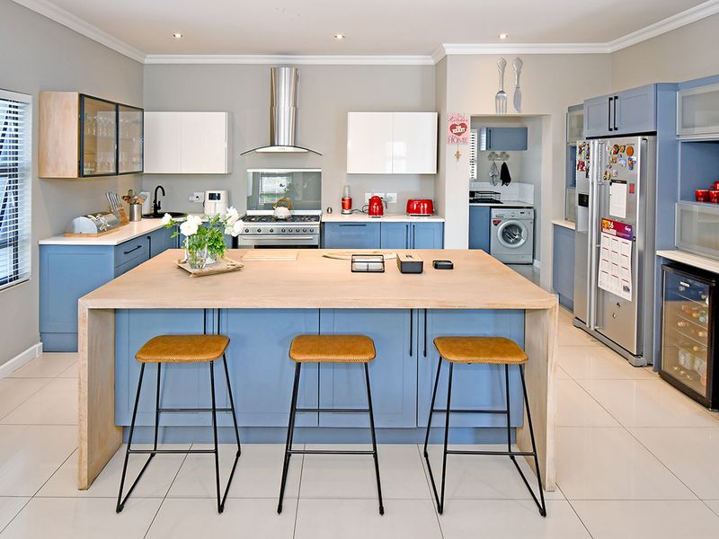 Modern kitchen featuring a large central island, blue cabinetry, stainless steel appliances, and a separate scullery area with laundry facilities.
