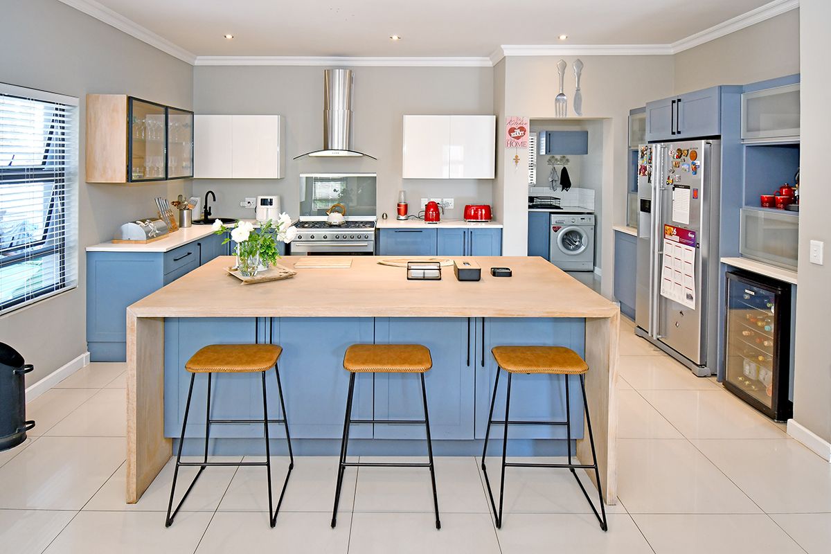 Modern kitchen featuring a large central island, blue cabinetry, stainless steel appliances, and a separate scullery area with laundry facilities.