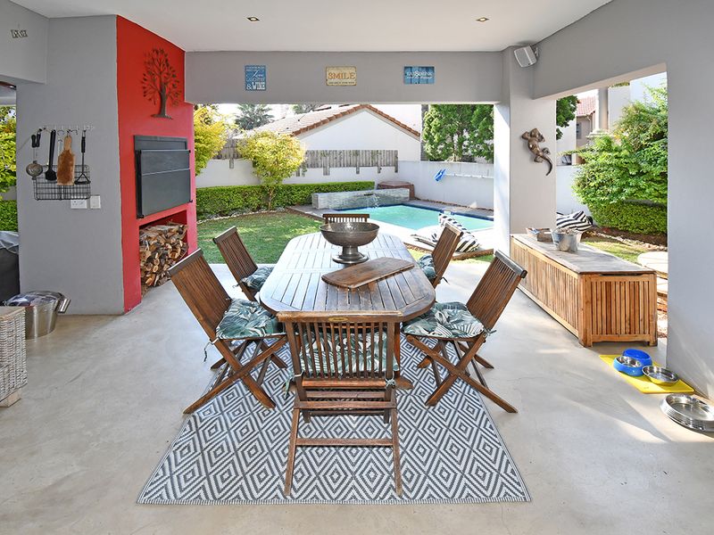 Covered outdoor patio featuring a built-in braai, concrete flooring, and direct access to the garden and swimming pool area.