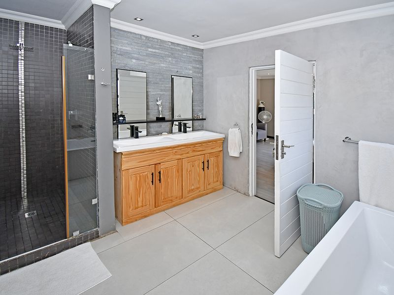 Modern bathroom featuring a double vanity with wooden cabinetry, a spacious walk-in shower with mosaic tiling, and a separate freestanding bathtub.