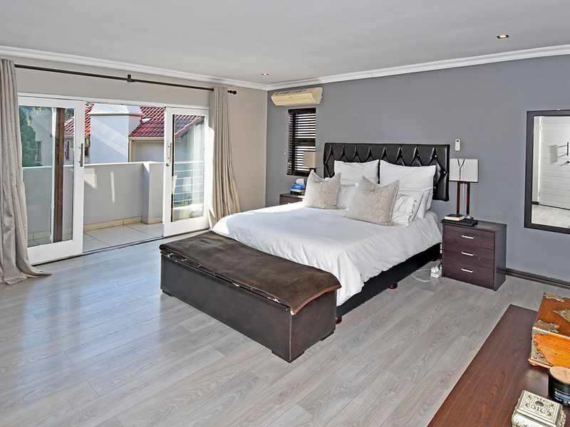 Spacious bedroom featuring light-toned laminate flooring, recessed lighting, and direct access to a private balcony through sliding glass doors.