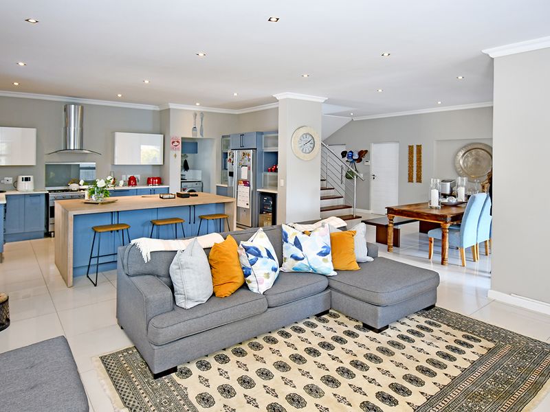 Spacious open-plan living area featuring a modern kitchen with a central island, dining space, and staircase, finished with neutral tones and tiled flooring.
