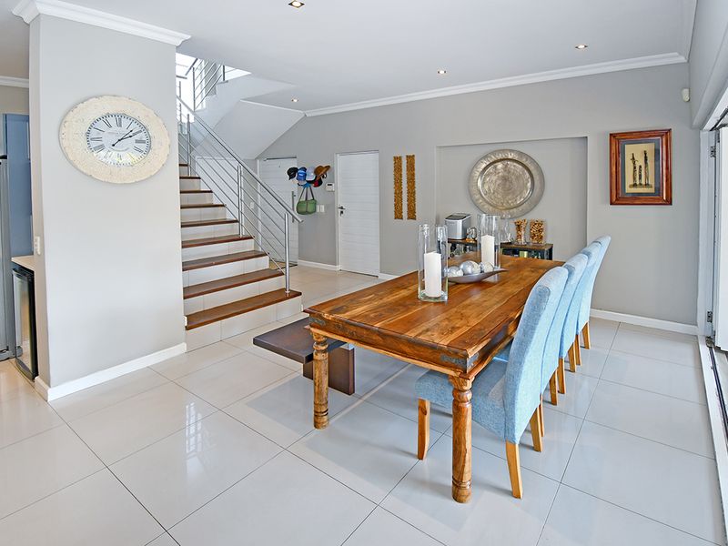 Open plan dining area featuring tiled floors, recessed lighting, and a modern staircase with stainless steel balustrades leading to the upper level.