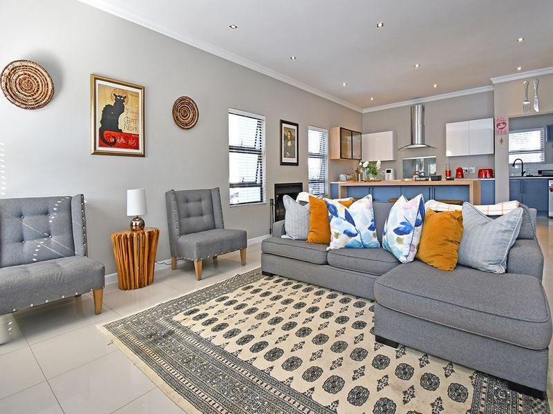 Spacious open-plan living area featuring a modern kitchen with island, recessed lighting, and tiled flooring, seamlessly flowing into the comfortable lounge space.