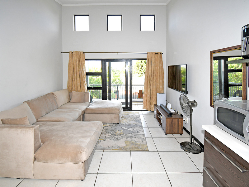 An open-plan living area featuring high ceilings, clerestory windows, tiled flooring, and direct access to a balcony through sliding glass doors.