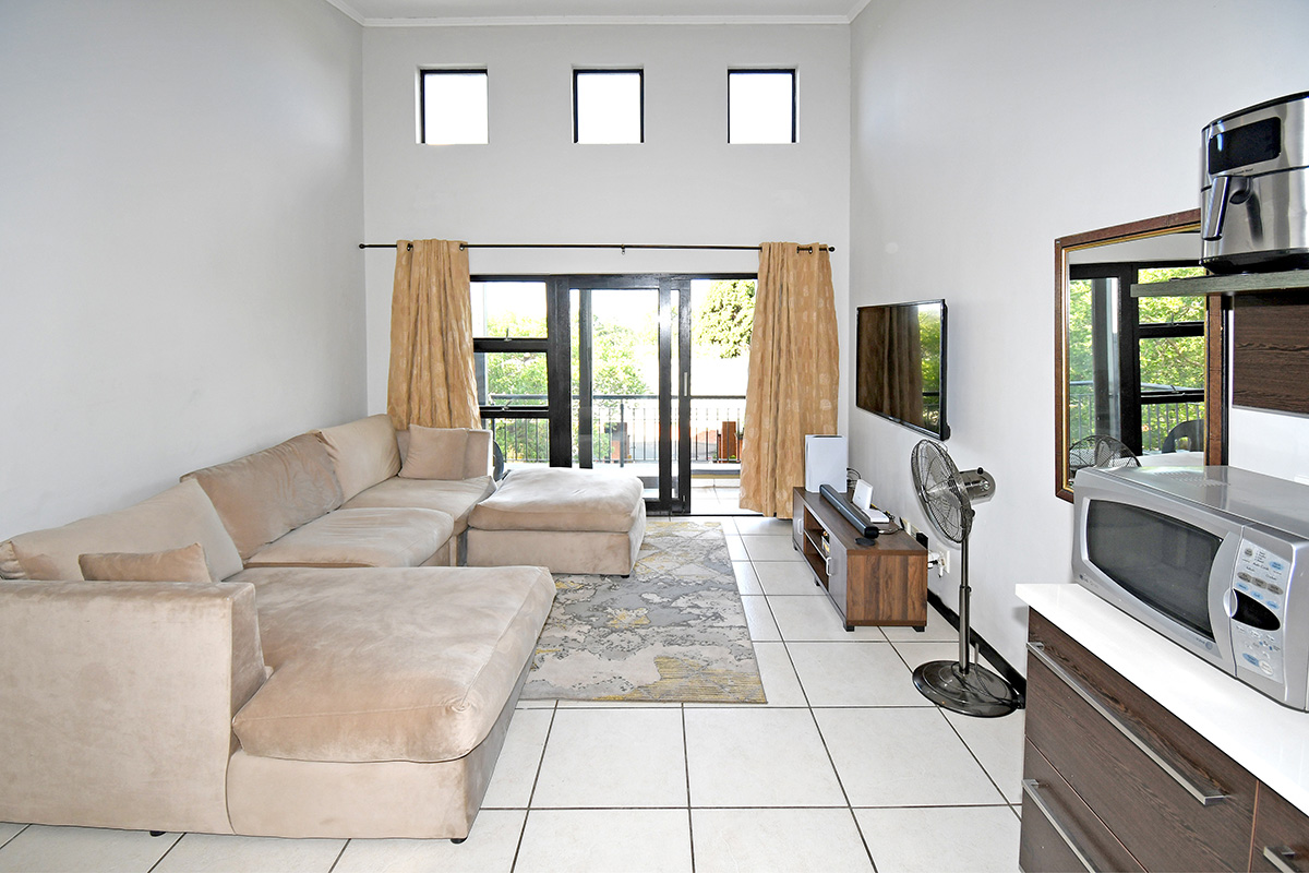 An open-plan living area featuring high ceilings, clerestory windows, tiled flooring, and direct access to a balcony through sliding glass doors.