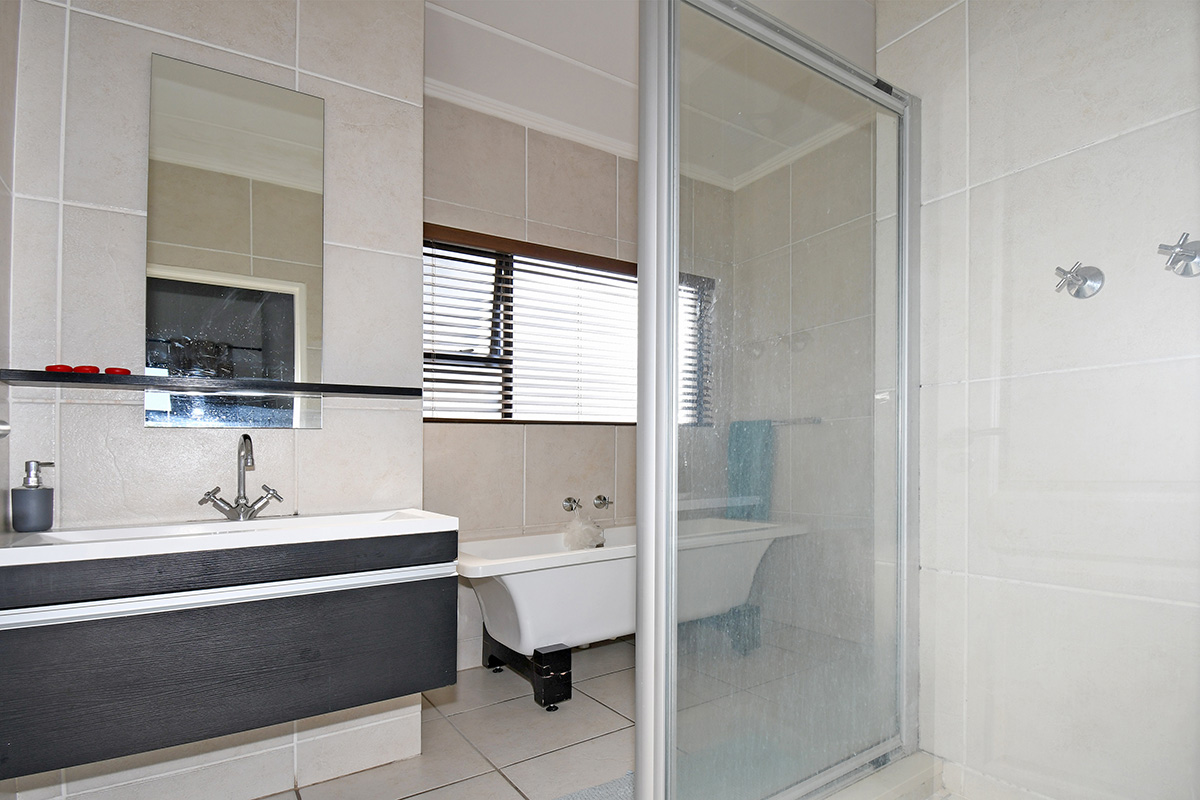 Modern bathroom featuring a wall-mounted vanity, a classic freestanding bathtub, and a separate glass-enclosed shower with neutral ceramic tiling throughout.