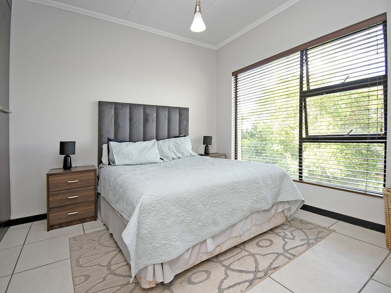 A well-lit bedroom featuring tiled flooring, built-in cupboards, and large windows fitted with venetian blinds.