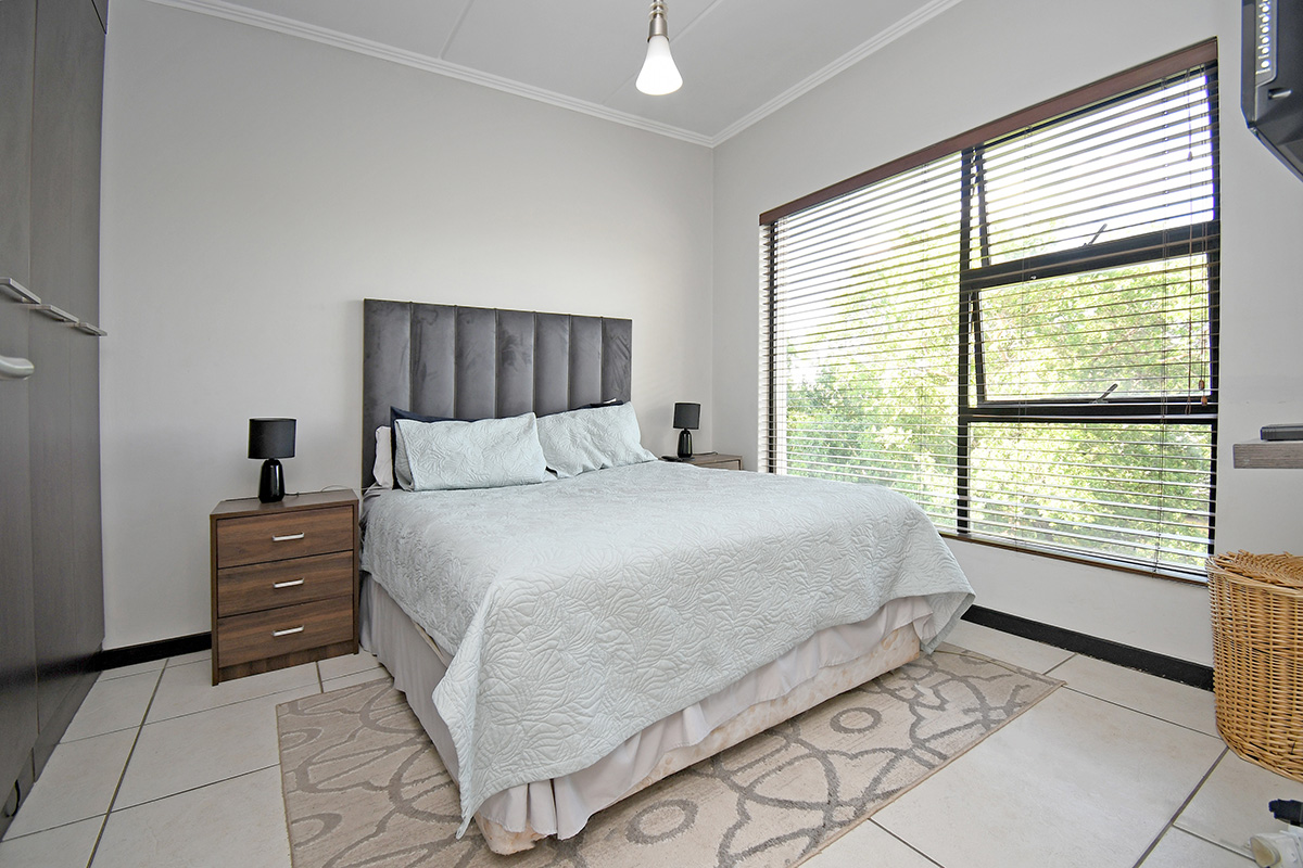 A well-lit bedroom featuring tiled flooring, built-in cupboards, and large windows fitted with venetian blinds.