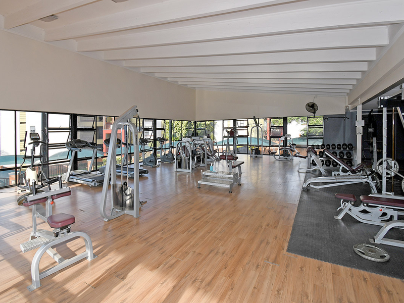 Spacious communal gym facility featuring exposed timber ceiling beams, large windows for natural light, and a combination of laminate and rubber flooring.