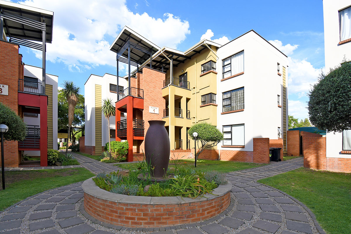 A well-maintained apartment complex courtyard featuring brick facades, landscaped gardens, paved pathways, and private balconies.