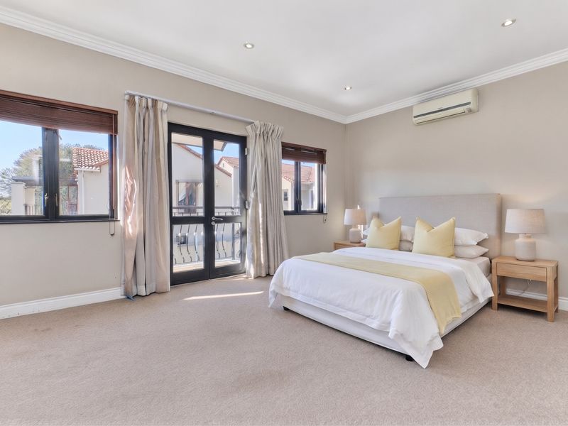 Spacious bedroom featuring neutral carpeting, crown molding, recessed lighting, a wall-mounted air conditioner, and double glass doors leading to an outdoor balcony.