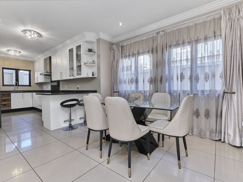 Modern open-plan kitchen and dining area featuring sleek white cabinetry, granite countertops, tiled flooring, and elegant crown molding throughout the space.