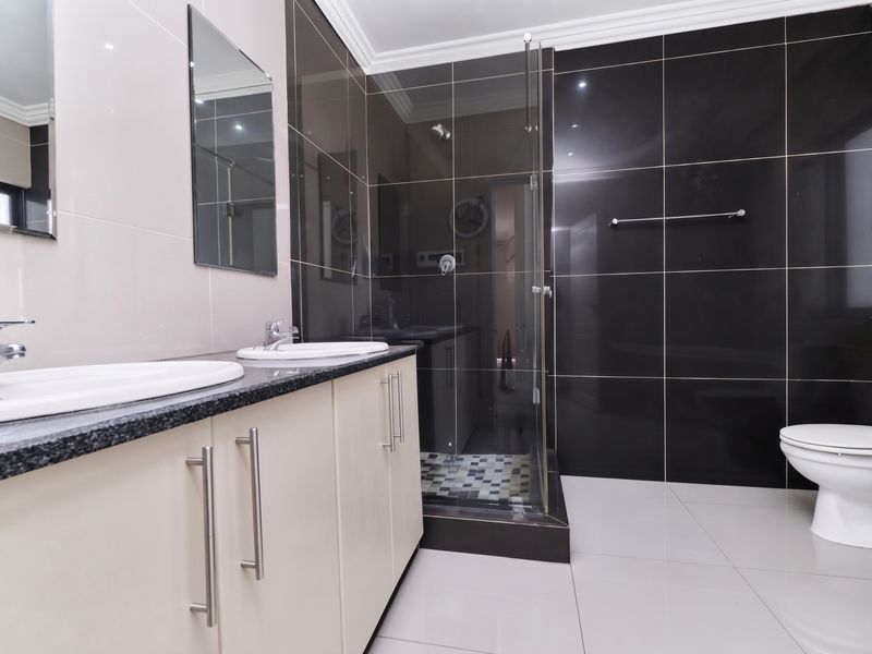 Modern bathroom featuring a double vanity with granite countertops, a glass-enclosed shower, and contrasting black and cream wall tiling.
