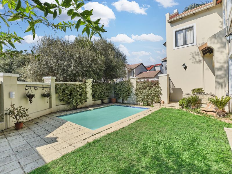 A private backyard featuring a swimming pool, paved patio area, and a well-maintained lawn enclosed by a boundary wall.