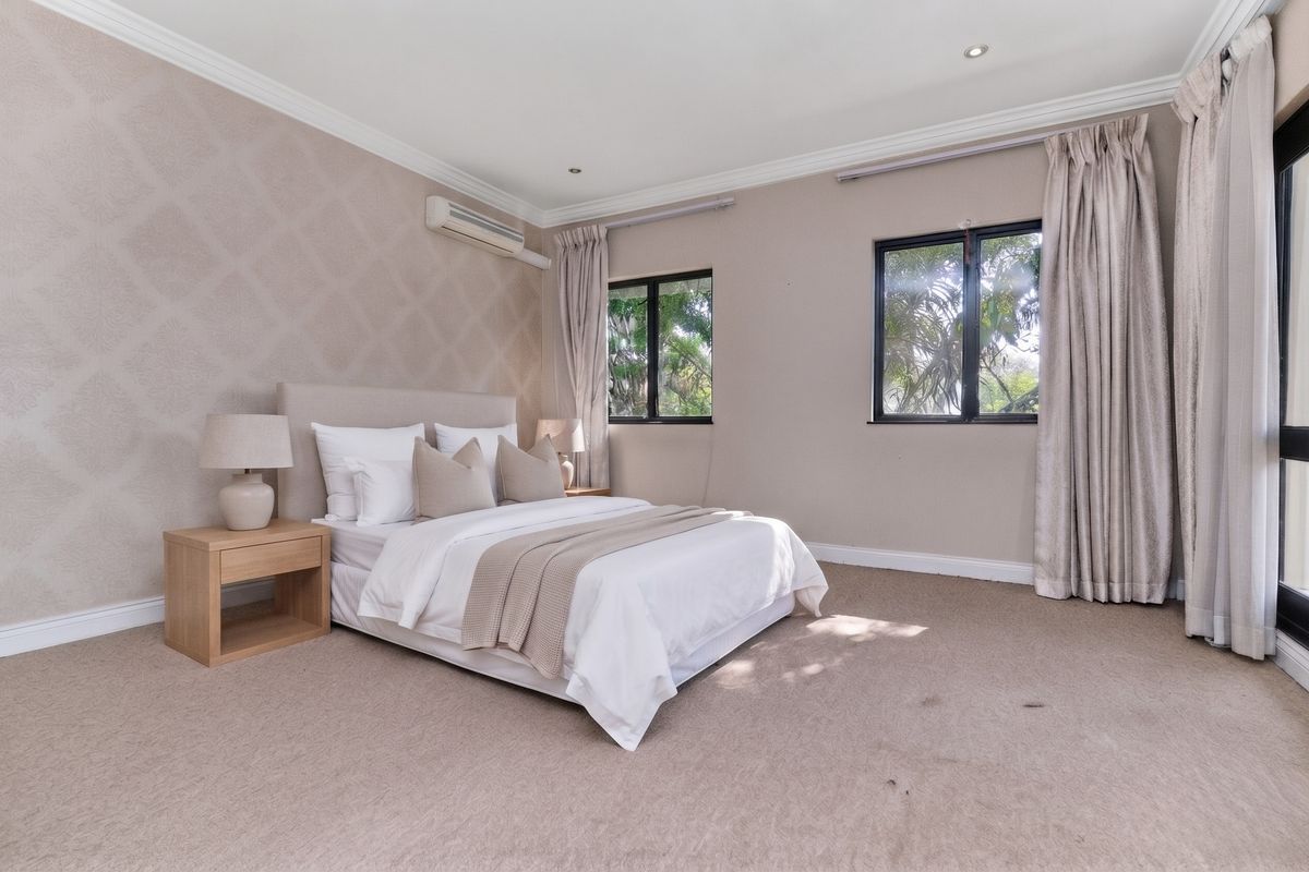 A spacious, well-maintained bedroom featuring neutral carpeting, crown molding, recessed lighting, and an integrated air conditioning unit.