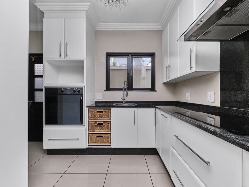Modern kitchen featuring white cabinetry, granite countertops, built-in oven, hob, extractor fan, and tiled flooring.